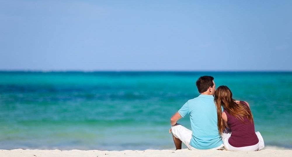 Honeymoon couple sitting together on a white-sand Zanzibar beach looking out over the turquoise Indian Ocean