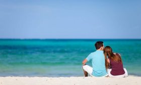 Honeymoon couple sitting together on a white-sand Zanzibar beach looking out over the turquoise Indian Ocean